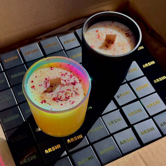 Two natural soy candles: one holographic jar and one black matte jar, adorned with rose petal decor with best hair oil
